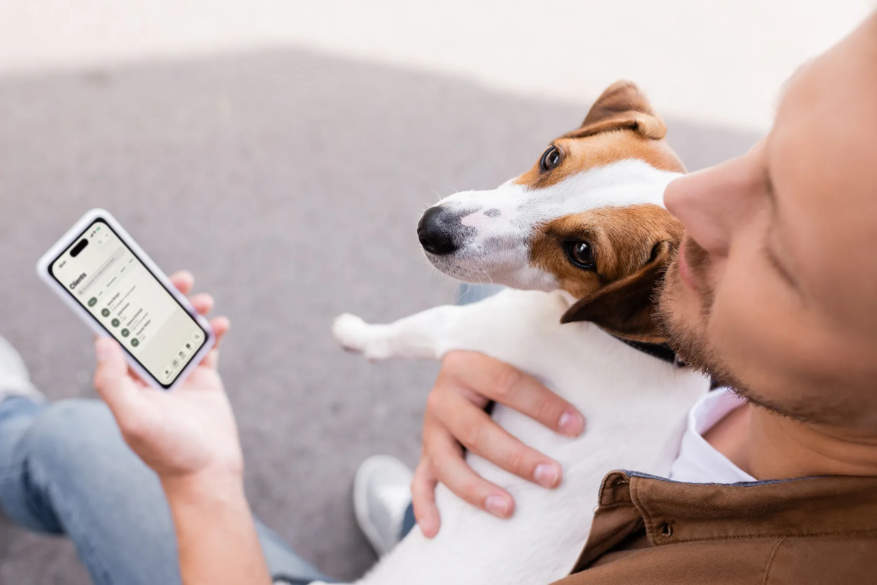 Un homme tient son Jack Russell dans les bras, la liste des clients de Dog Walkers ouverte sur son iPhone.